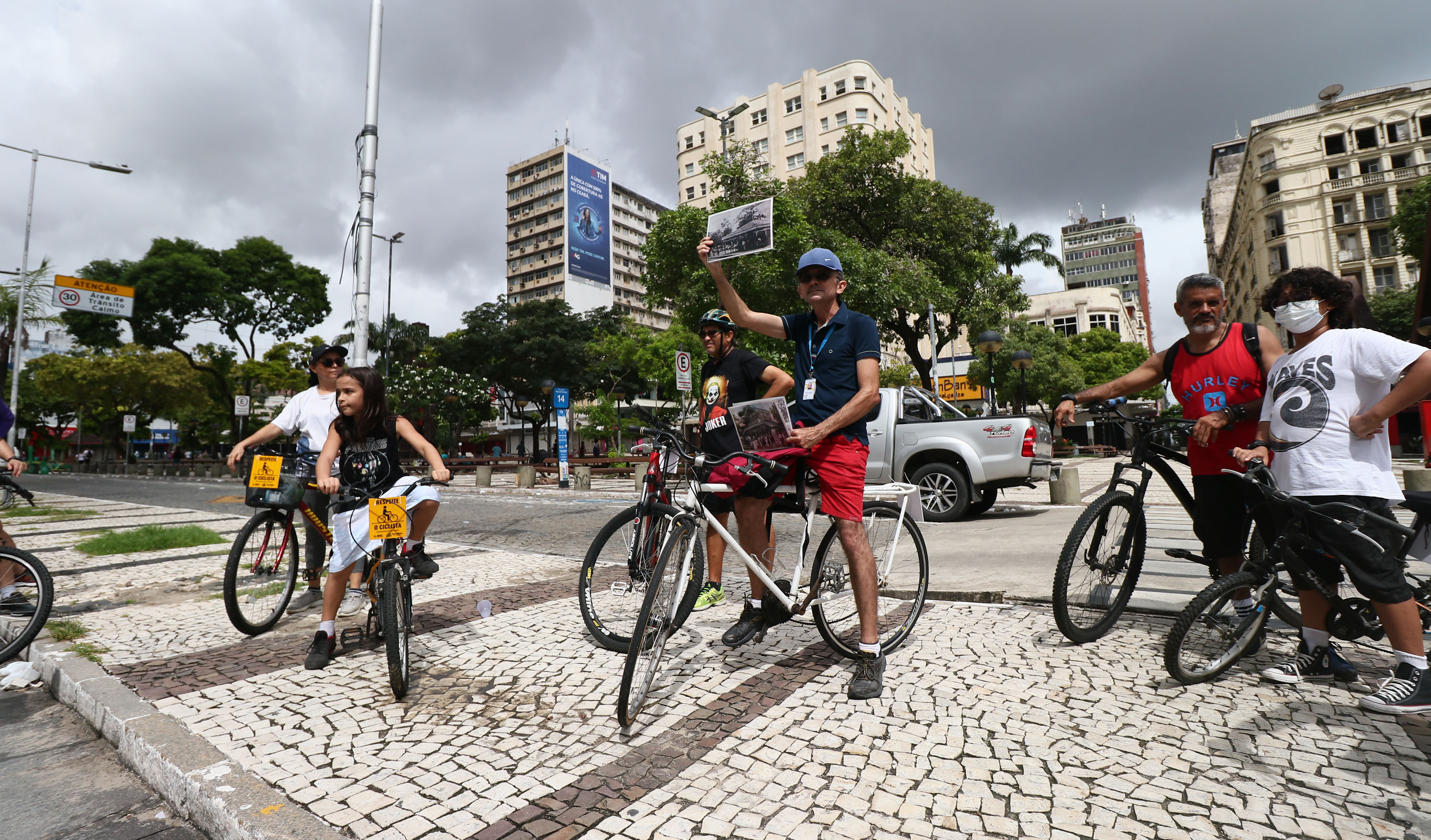 instrutor da ciclofaixa cultural mostra uma foto antiga da praça do ferreira no momento em que o grupo de ciciistas está na praça